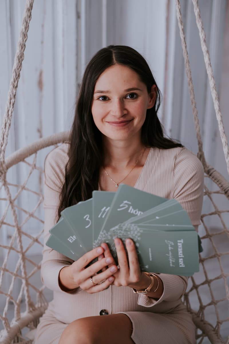 hosszú hajú nő mosolyog és kezében zsálya zöld színű újszülött mérföldkőkártyákat tart 