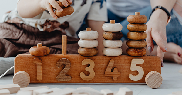 natúr színű fa montessori kisvonat toronyépítővel játszik egy kisgyermek